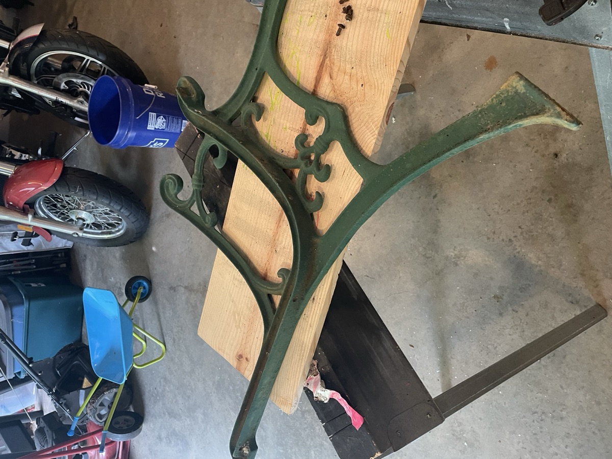 The original green cast-iron bench ends resting on a workbench, paint chipped and worn
