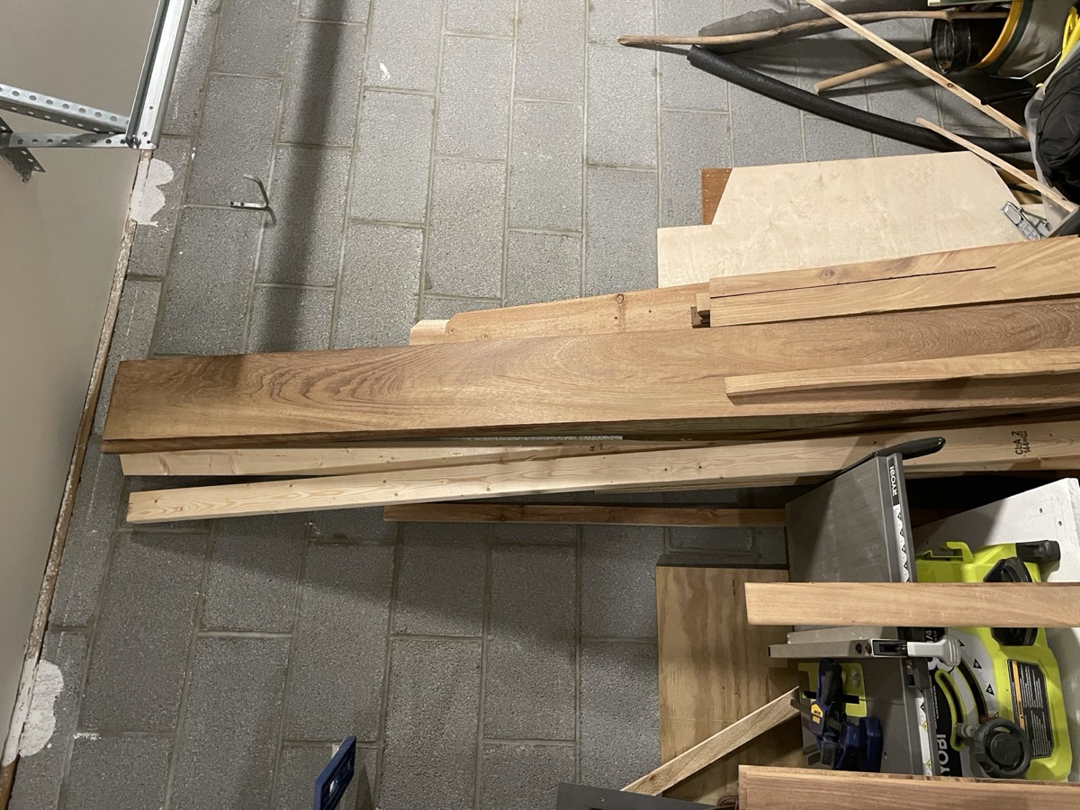 Rough-sawn African teak boards leaning against a cinder-block workshop wall