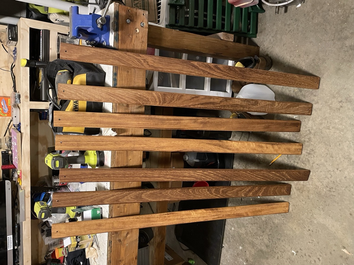 Seven finished teak slats lined up against a workbench, rich with color after teak oil