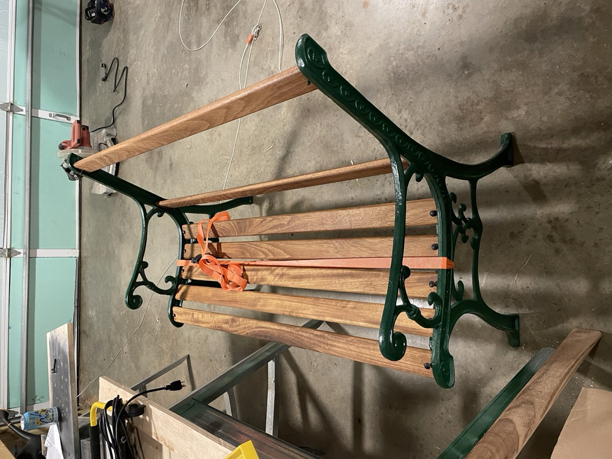 The reassembled bench: freshly painted green cast-iron frame with new teak slats, held by an orange strap